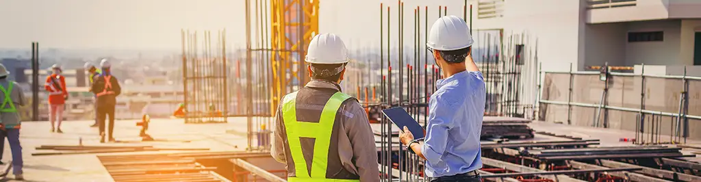 Two Men In Hard Hats Pointing At Area Of Construction Site