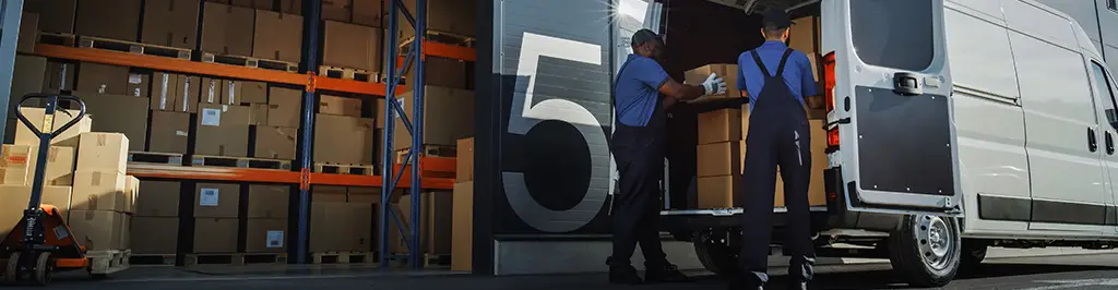 Two Men Loading White Van Next To Warehouse